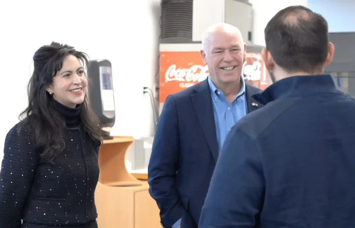 Governor Gianforte, Secretary Jacobsen celebrate another year of record business creation 4 Two people in business attire smile and talk with a third person whose back is to the camera, inside a room with office equipment and a Coca-Cola machine—discussing record business growth and business creation strategies.
