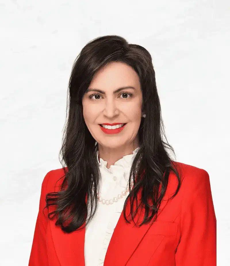 Woman with long dark hair wearing a red blazer, white blouse, and pearl necklace, smiling in front of a plain white background—Secretary Christi Jacobsen highlighted Montana business growth in June 2023.