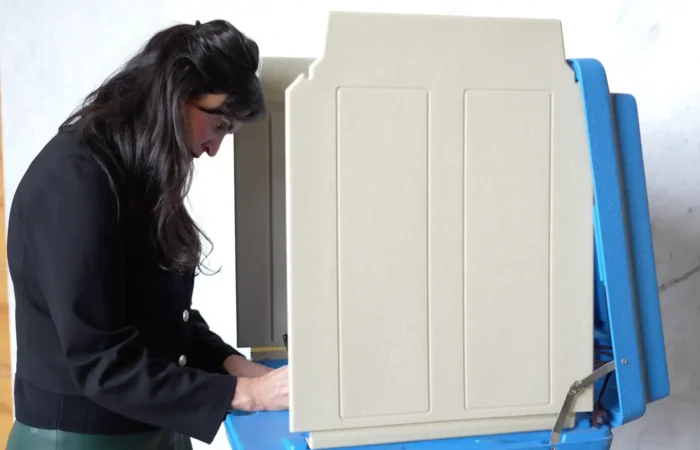 Secretary Christi Jacobsen: 'Nearly 425,000 absentee ballots received entering Election Day' 4 A woman with long dark hair stands at a beige voting booth on Election Day, looking down as she marks her ballot. The booth provides privacy for her as she votes.