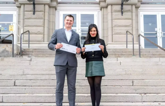 Montana Secretary of State Christi Jacobsen votes in 2024 Election, reminds Montanans of voter resources 6 A man in a gray suit and a woman in a black jacket and green skirt stand on stone steps outside a large building, both smiling and holding certificates or voter resources from the Montana Secretary of State.