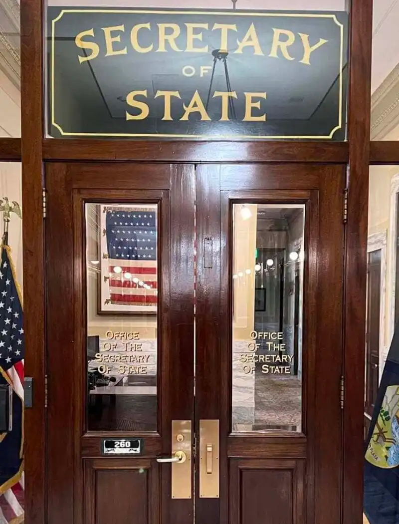 Secretary Christi Jacobsen dispels attacks on Montana’s commonsense voting laws 7 Glass doors labeled Secretary of State lead to an office, where U.S. and Montana flags stand proudly. Inside, the American flag and framed artwork are visible—reflecting Christi Jacobsen’s commitment to commonsense voting in Montana.