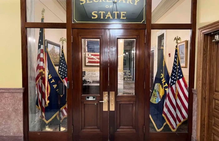 Montana Secretary of State's Office sees slight increase in candidate filings 8 A wooden doorway with glass panels leads to the Montana Secretary of State office. American and Montana state flags stand on both sides. The office sign and a reflection of another flag are visible in the glass, where candidate filings and elections take place.