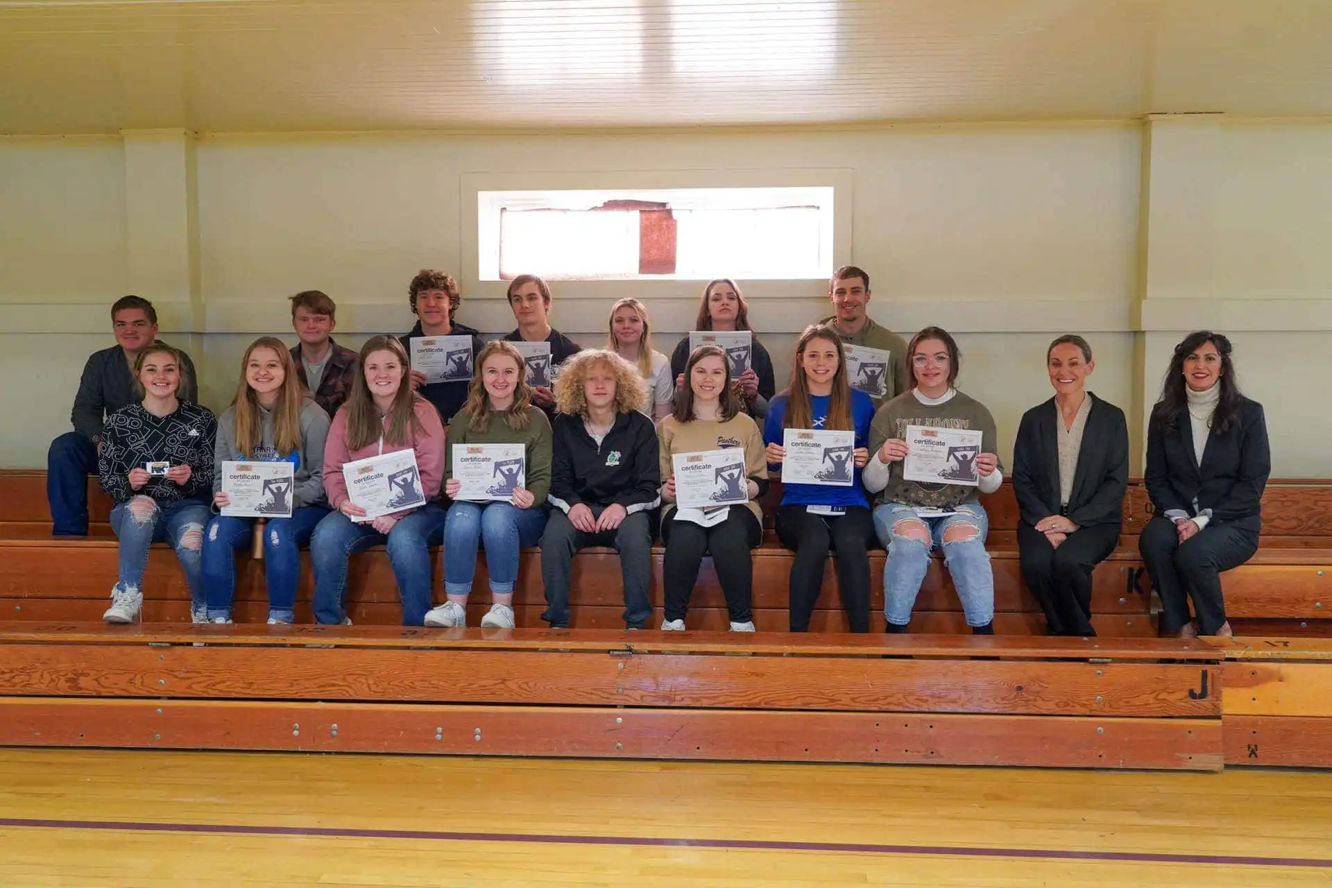 Sheridan High School students, staff honored for participation in US Constitution Contest 16 A group of students and two adults sit on wooden bleachers indoors at Sheridan High School. Many of the students, holding certificates from the US Constitution Contest, smile at the camera as light enters through a window behind them.