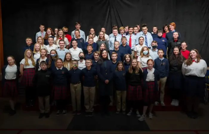 Secretary Jacobsen delivers Constitutions to St. Andrew School, takes questions from students 5 A large group of St. Andrew School middle school students in uniforms pose for a class photo in rows against a dark backdrop, with some students smiling and others looking serious, as Secretary Jacobsen observes nearby.