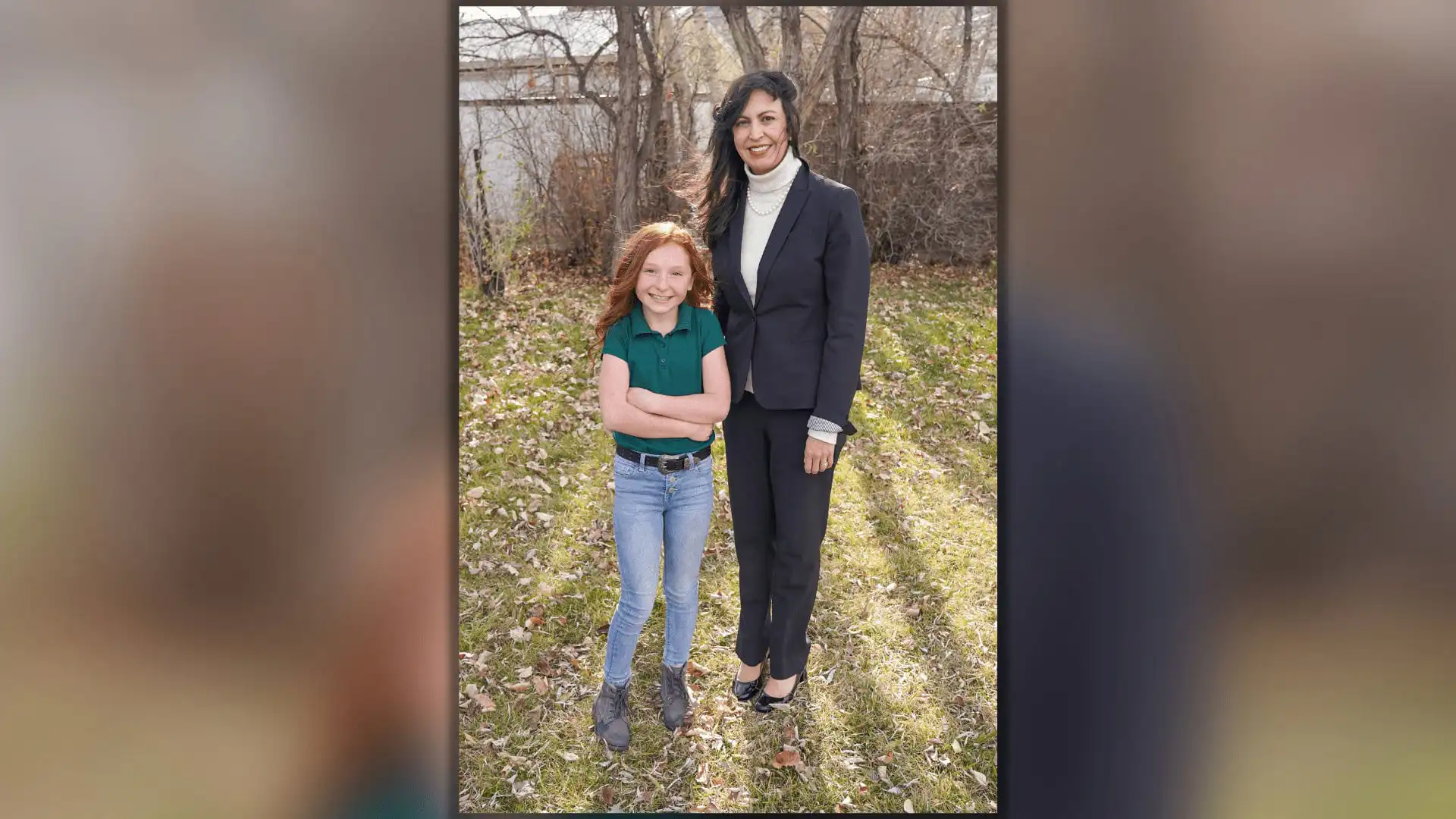Song from The Way Christian School student wins US Constitution Contest 14 A woman in a dark suit stands outside on grass next to a smiling young girl with long red hair, wearing a green shirt and blue jeans. They appear to be celebrating the US Constitution Contest at The Way Christian School, with trees and a wooden fence behind them.