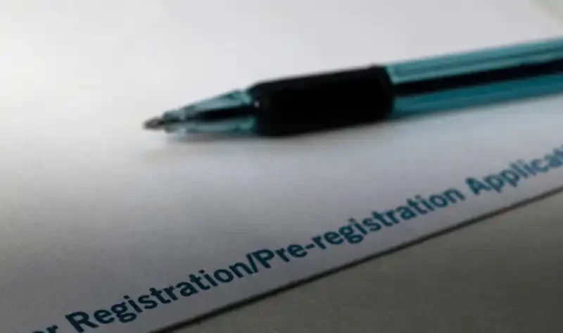 A blue pen rests on a sheet of paper with the partially visible text Registration/Pre-registration Application, provided by the Montana Secretary of State, printed in blue in the bottom-right corner.