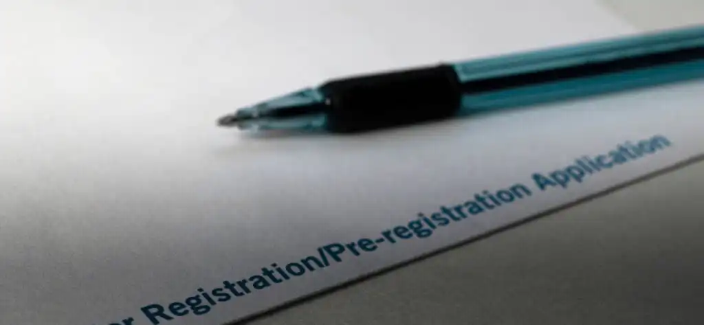 A blue pen rests on a sheet of paper with the partially visible text Registration/Pre-registration Application, provided by the Montana Secretary of State, printed in blue in the bottom-right corner.