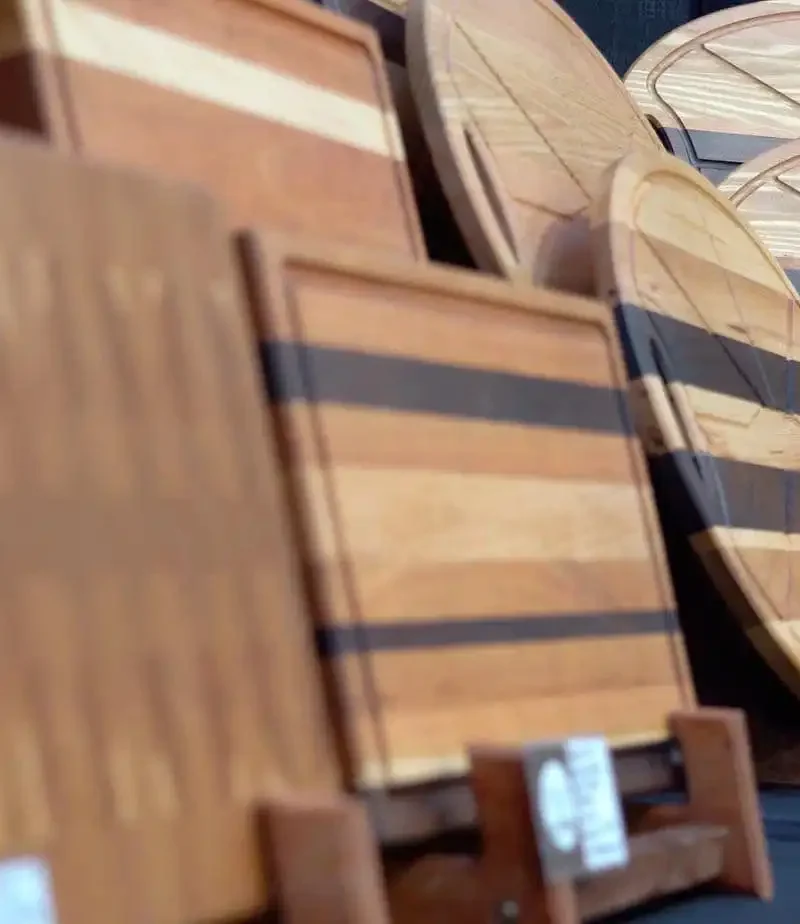 Several wooden cutting boards and serving trays by Montana Block, featuring unique shapes and wood patterns, are displayed upright on a black tablecloth at a craft fair as part of the Made in Montana program.