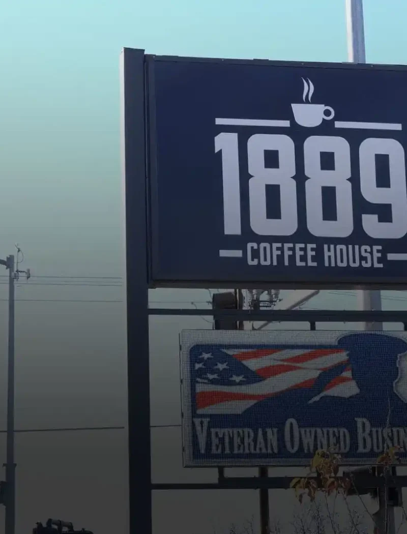 A large outdoor sign reads 1889 Coffee House above another sign stating veteran-owned, featuring an American flag and soldier silhouette. A street sign for Laramie St. appears in the background of this Montana business.