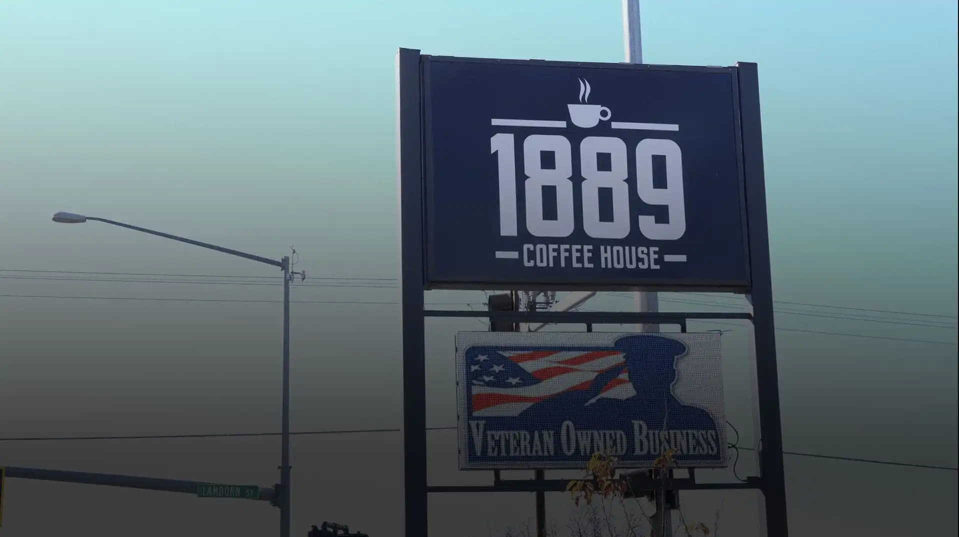 A large outdoor sign reads 1889 Coffee House above another sign stating veteran-owned, featuring an American flag and soldier silhouette. A street sign for Laramie St. appears in the background of this Montana business.