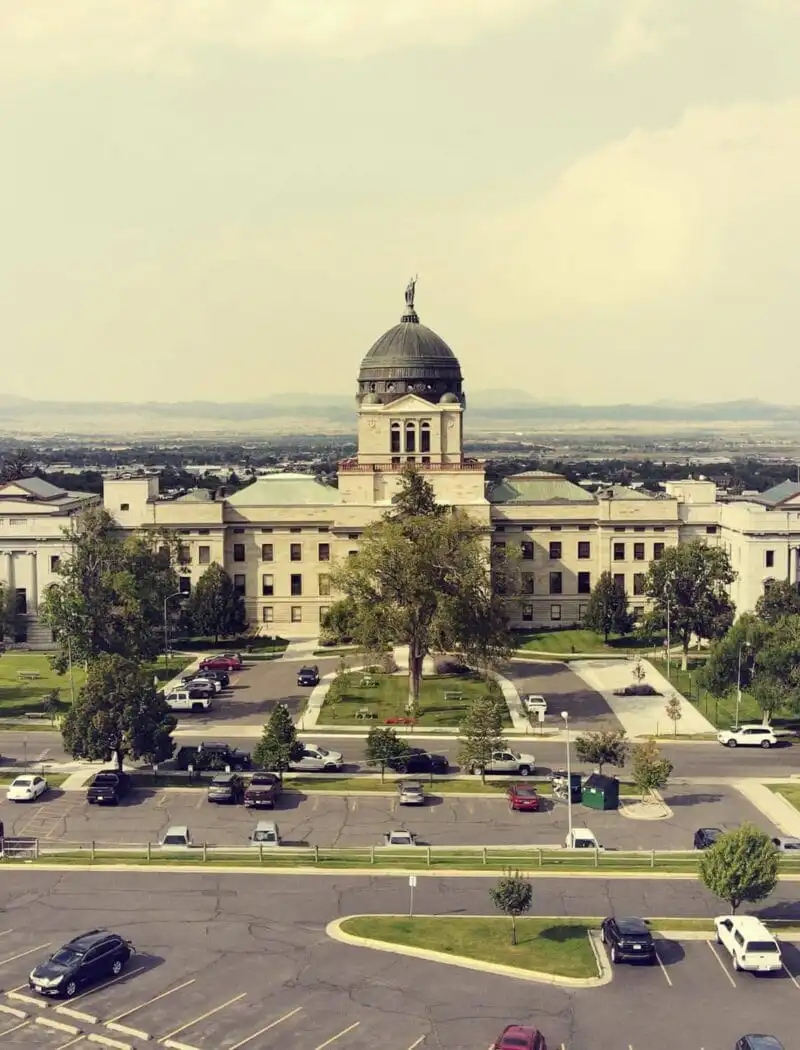 Secretary Christi Jacobsen, state officials to welcome Halloween trick-or-treaters to State Capitol 1 A large government building with a central dome and flag on top, surrounded by trees and lawns, offers business services; parked cars line the front as mountains rise in the background beneath a hazy sky.