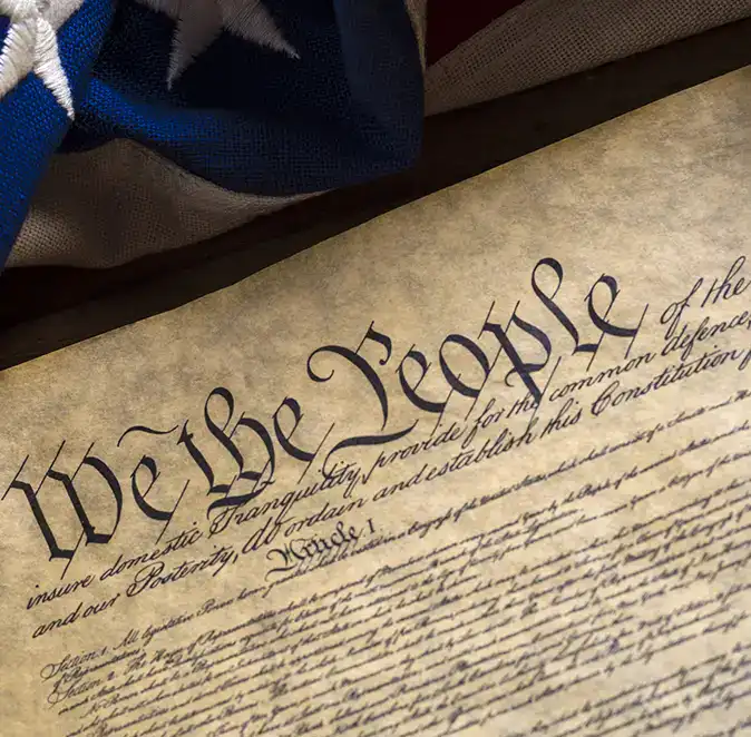 A close-up of the United States Constitution showing the words We the People, with part of an American flag visible in the background, highlighting the importance of civics and youth engagement in shaping our nation’s future.